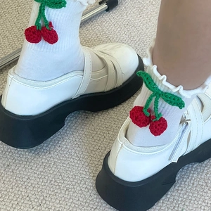 Gros plan de chaussettes blanches à volants avec cerises crochetées et chaussures