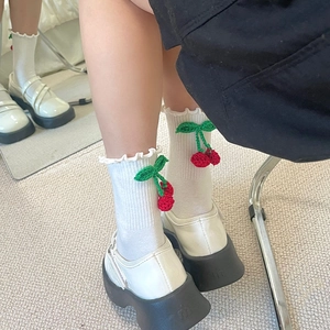 Détail de chaussettes blanches en tricot avec bordure ondulée et breloques cerises en 3D