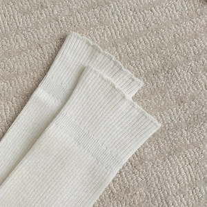 Detail shot of white ribbed calf socks with elegant ruffled edges on a beige carpet