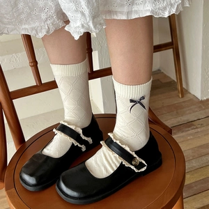 Detail of white diamond-knit socks with black and white plaid bow and lace Mary Jane shoes