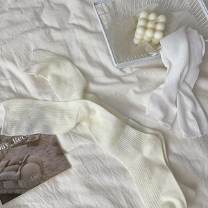 Detail of ribbed knit long socks in cream white and pure white colors on textured fabric