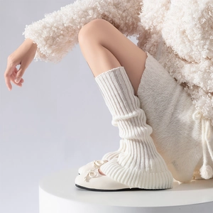Close-up of cream knit leg warmers with vertical ribs on a minimalist display