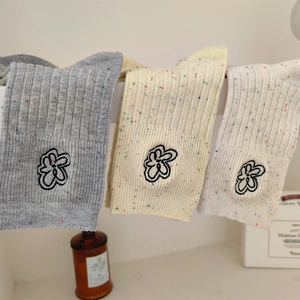 Dettaglio della trama a maglia di calze ricamate con fiori in grigio, giallo e panna