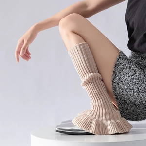 Detail of beige ribbed knit leg warmers with ruffle edges paired with silver shoes
