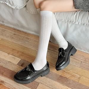 Close-up of white ribbed knit crew socks paired with black patent leather platform loafers