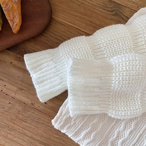 Detailed close-up of cream knit leg warmers showing intricate hollow diamond patterns