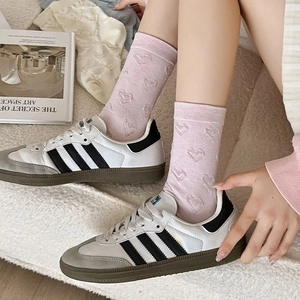 Pink mid-calf socks with 3D embossed heart pattern shown with sneakers on soft rug