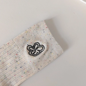 Dettaglio ravvicinato di calze in maglia crema con puntini colorati e ricamo floreale nero