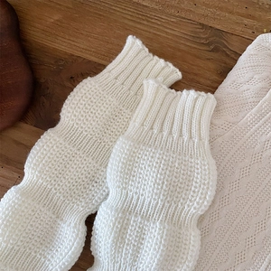 Detail view of white cable knit leg warmers with bubble texture on wooden background