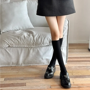 Detail of black patent leather loafers with vertical ribbed socks on wooden floor