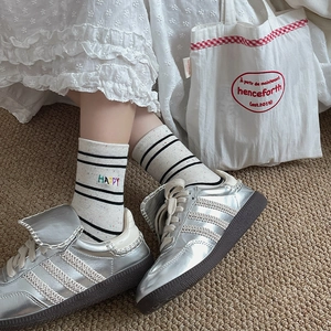 Detail of cotton crew socks with HAPPY embroidery and silver sneakers on a rug