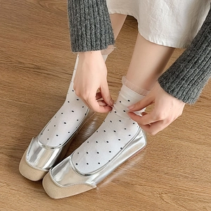 Top view of silver flat shoes with beige toe and white polka dot mesh socks on wood floor