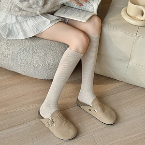 Close-up of beige ribbed knit calf socks paired with khaki buckle suede slippers