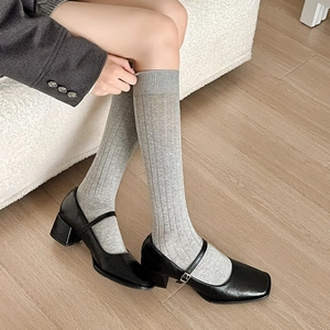 Close-up of grey vertical striped knit calf socks paired with black Mary Jane shoes