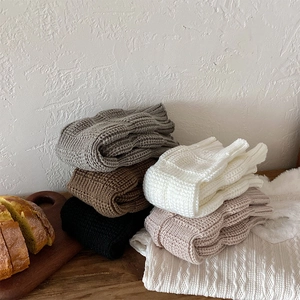 Close-up of thick knit leg warmers in neutral colors stacked on a wooden surface