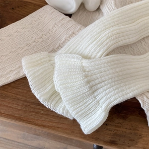 Close-up of white knitted leg warmers with delicate lace patterns and ribbed texture