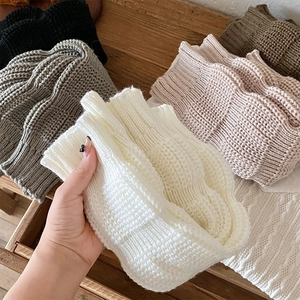 Detail of chunky cable-knit leg warmers showing soft wool texture in various neutral colors