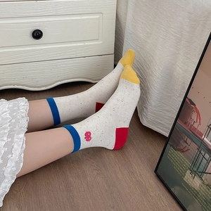 Detail of colorful speckled cotton socks with red fruit embroidery on wooden floor
