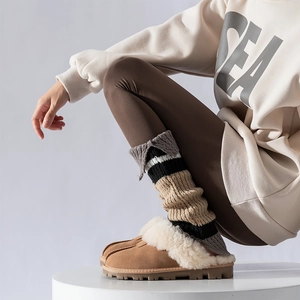 Detail of striped knitted leg warmers paired with khaki faux shearling slippers for winter