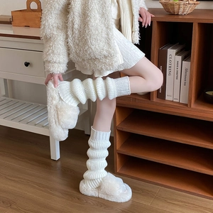 Close-up of white chunky knit leg warmers paired with plush faux fur slippers in a home setting
