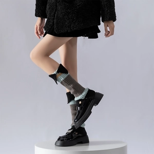Detail shot of striped knitted leg warmers with buttons paired with loafers and black coat