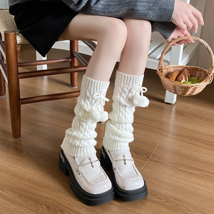 Detail of white cable knit leg warmers with plush pom-poms and ribbon bows