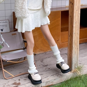 Detailed knit texture of white ballet style leg warmers with cream platform shoes
