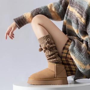Close-up of cable knit leg warmers with pom-poms and warm brown suede platform boots