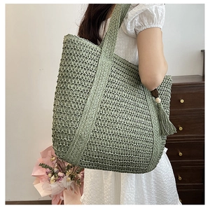 Detail of green hand-woven straw tote bag with long tassels and wooden beads decoration