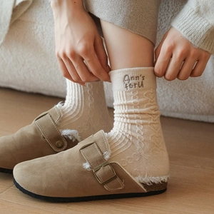Detail of beige wool socks with letter embroidery and brown suede sheepskin clogs