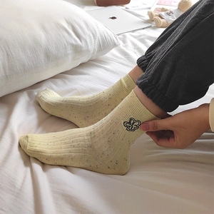 Dettaglio di calzini beige con ricamo floreale e maglia maculata colorata morbida