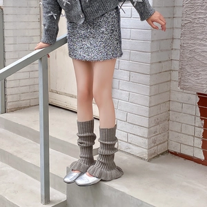 Close-up of ballet-style taupe knitted leg warmers styled with silver ballet flats