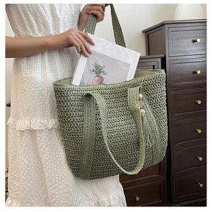 Detail of green straw woven tote bag with tassel and wooden bead charm on a wooden background