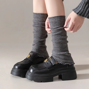 Close-up of black leather platform loafers with gold hardware and gray knitted leg warmers