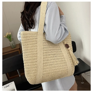 Detail of beige straw tote bag featuring decorative wooden beads and long tassels