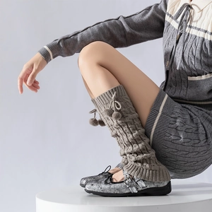Detail of grey cable knit leg warmers with pompoms paired with silver Mary Jane shoes