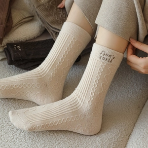 Detailed close-up of beige wool socks featuring letter embroidery and ribbed knit texture