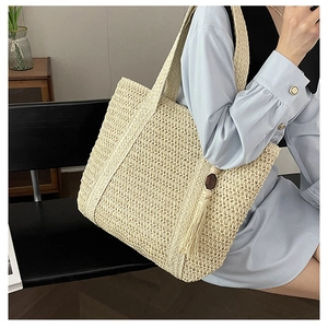 Close-up of beige woven straw tote bag with wood bead tassel detail and wide shoulder strap