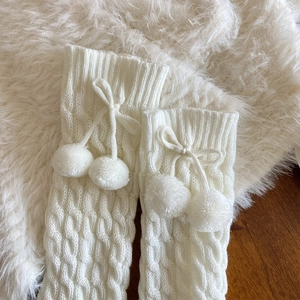 Detail of white knit leg warmers with cable pattern and fluffy pom-pom decorations