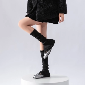 Detail of black ribbed knit leg warmers paired with silver ballet flats on a white pedestal