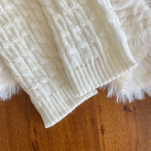 Detail of white cable knit leg warmer with ribbed cuff and thick textured pattern