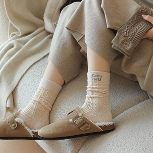 Detail of wool socks with heart knit patterns and letter embroidery worn with clogs