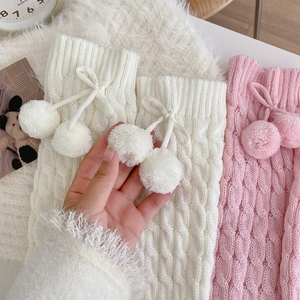 Detail of cable knit leg warmers with fluffy pom-poms and cute bow ties in white and pink