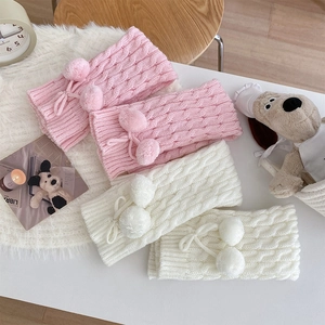 Detail of pink and white cable knit leg warmers with pom-poms on a cozy white rug