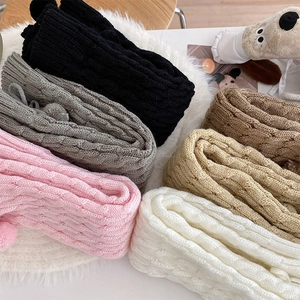 Detail of cable knit leg warmers in various colors featuring decorative pom-poms