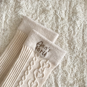 Macro detail of cream wool socks featuring heart jacquard patterns and embroidery