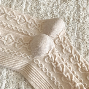 Macro shot of cream wool socks featuring heart jacquard patterns and cable knit textures