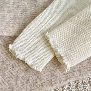 Detailed macro view of the cream white ribbed knit leg warmers with elegant frill edges