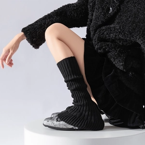 Ballet style black knit leg warmers with vertical stripes on a white platform