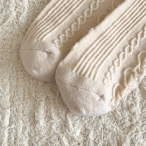 Detailed macro view of cream wool socks featuring vertical ribs and cable knit textures